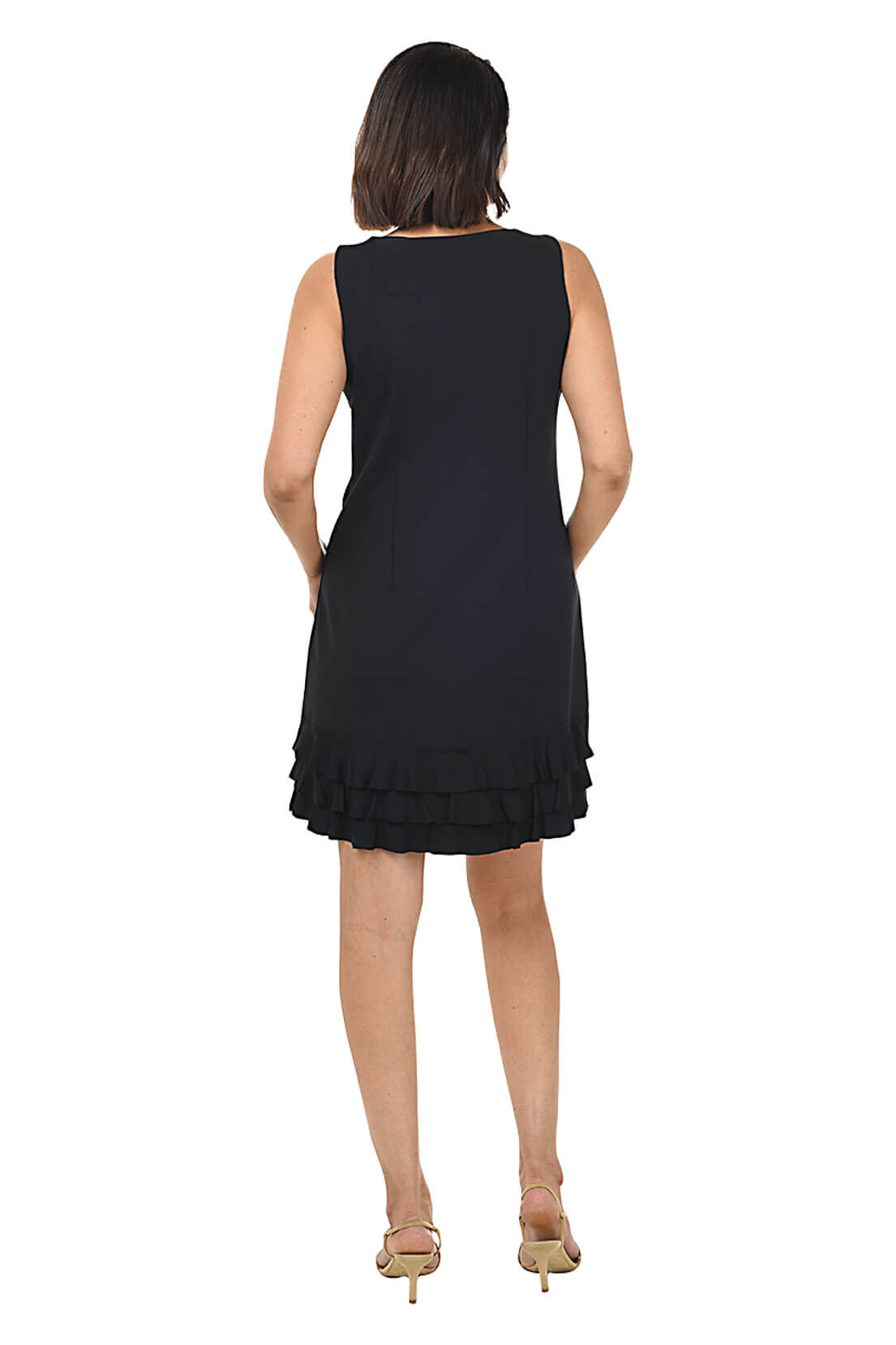 A woman standing and posing in a sleeveless black dress with a scoop neckline and triple ruffle detail at the hemline. Back shot.