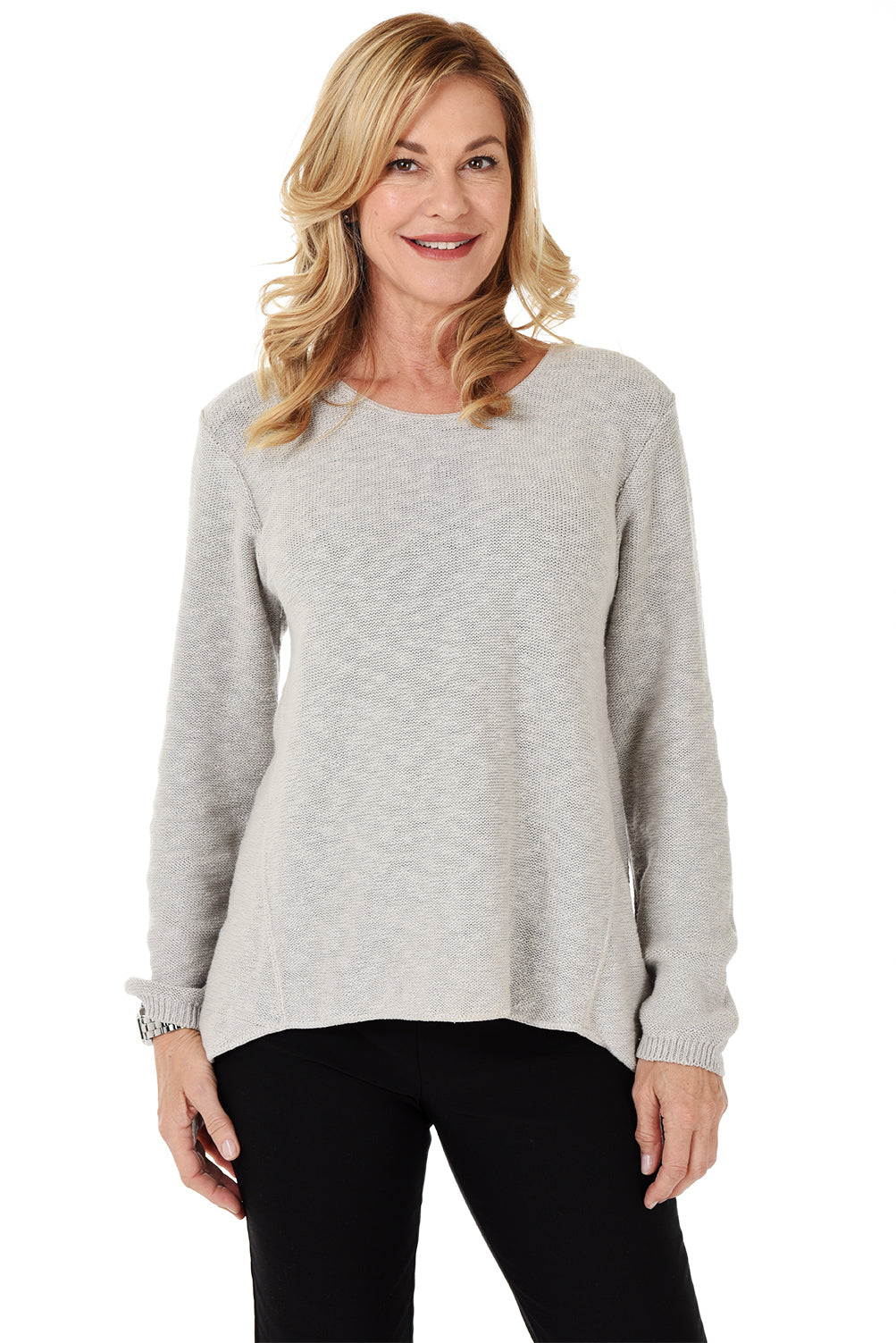 A woman wearing a long sleeve light grey cotton scoop neck sweater, with a seam down the front and white pants.
