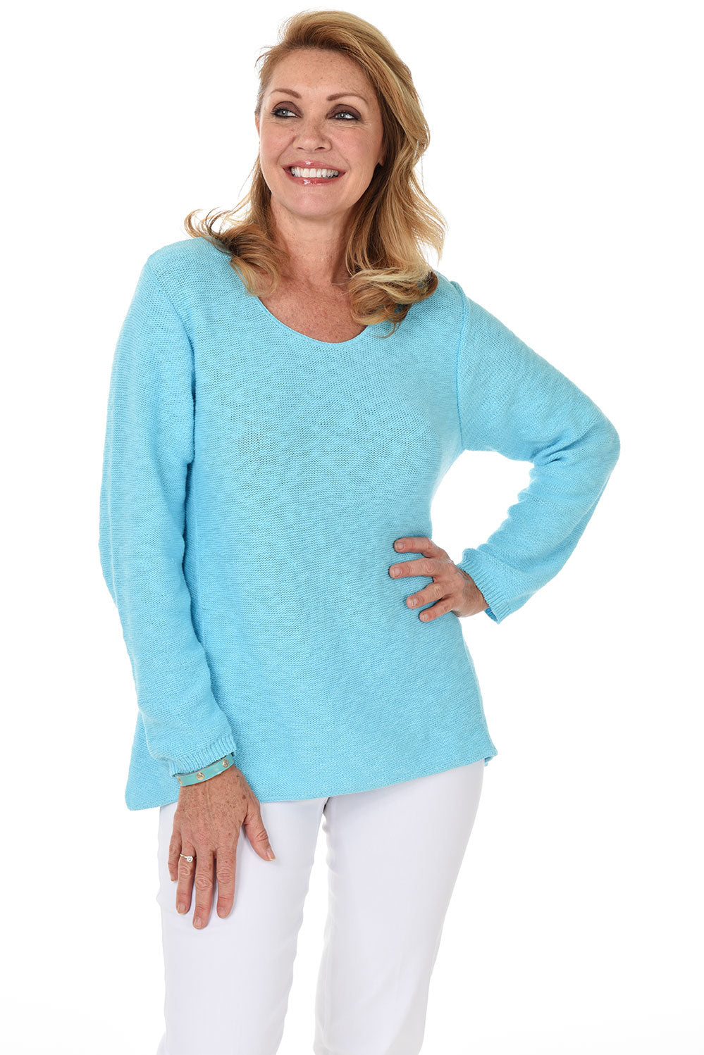 A woman wearing a long sleeve turquoise cotton scoop neck sweater, with a seam down the front and white pants.