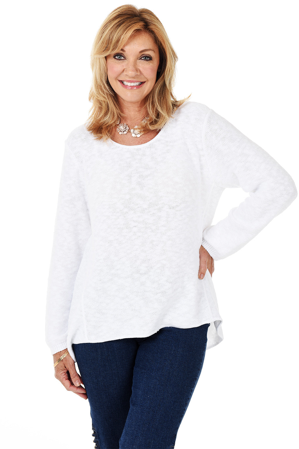 A woman wearing a long sleeve white cotton scoop neck sweater, with a seam down the front and denim pants.