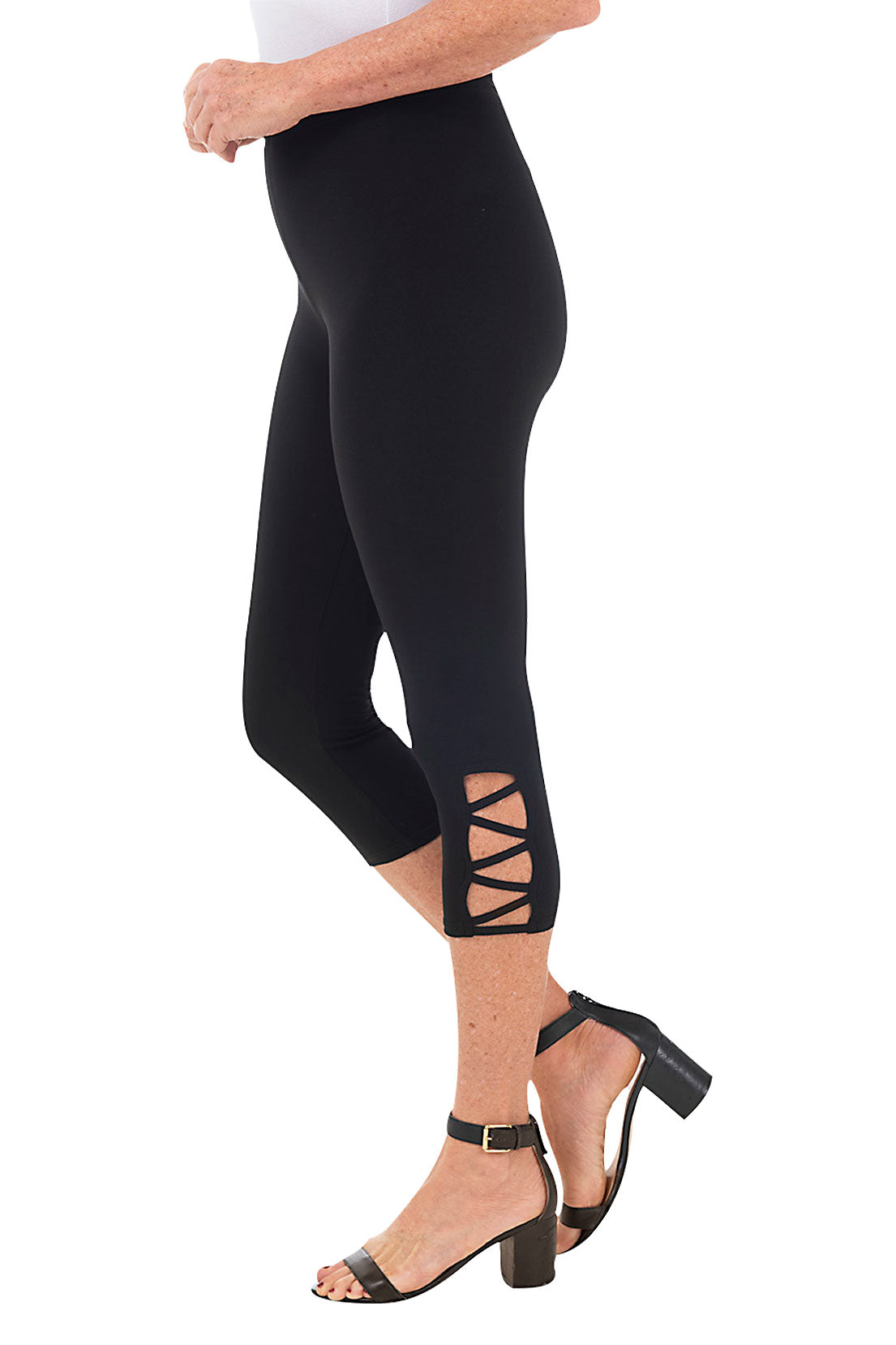 A pair of black capri leggings with lattice detailing on the hemline, paired with a white tunic and heels. Side shot.