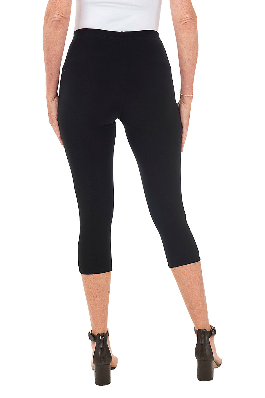 A pair of black capri leggings with lattice detailing on the hemline, paired with a white tunic and heels. Back shot.