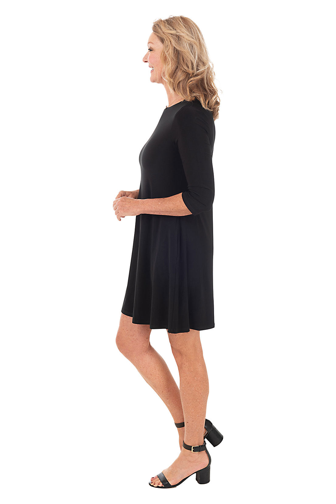 A model wearing a long sleeve black dress with a scoop neckline, dual side pockets, and a straight hemline. Side shot.