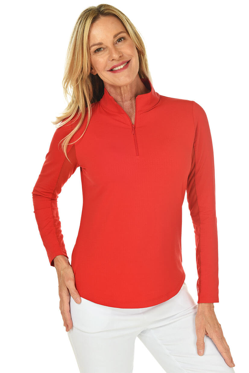 A woman smiling and wearing a long-sleeved red sun shirt with a mock-neck collar and a pair of white pants.