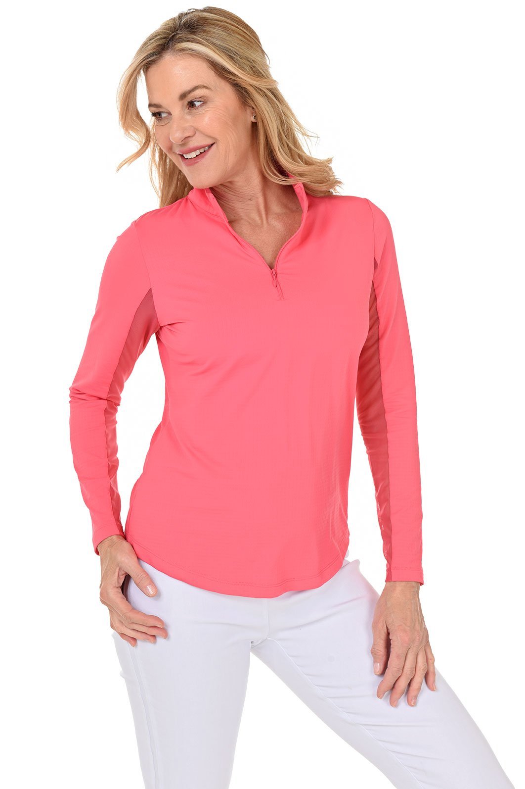 A woman smiling and wearing a long-sleeved watermelon sun shirt with a mock-neck collar and a pair of white pants.