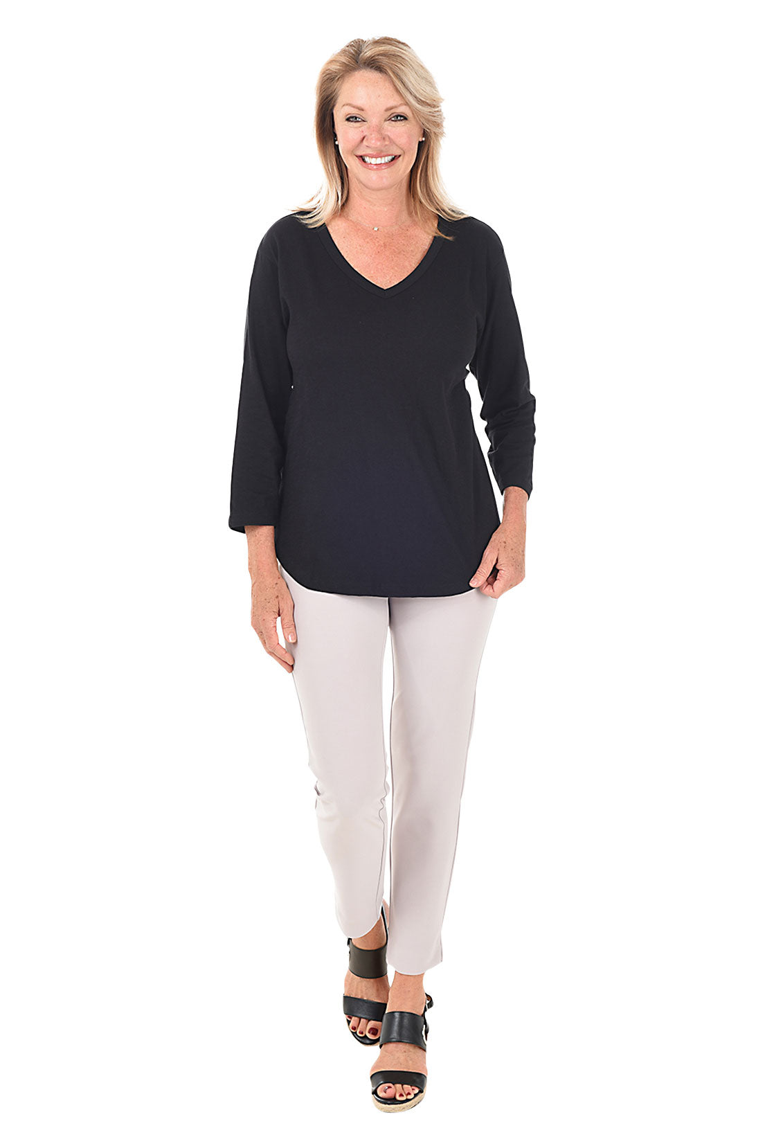 A full length shot of a model wearing a pair of white microfiber pull-on ankle pants with an elastic waistband, displayed on a model wearing black top and heels