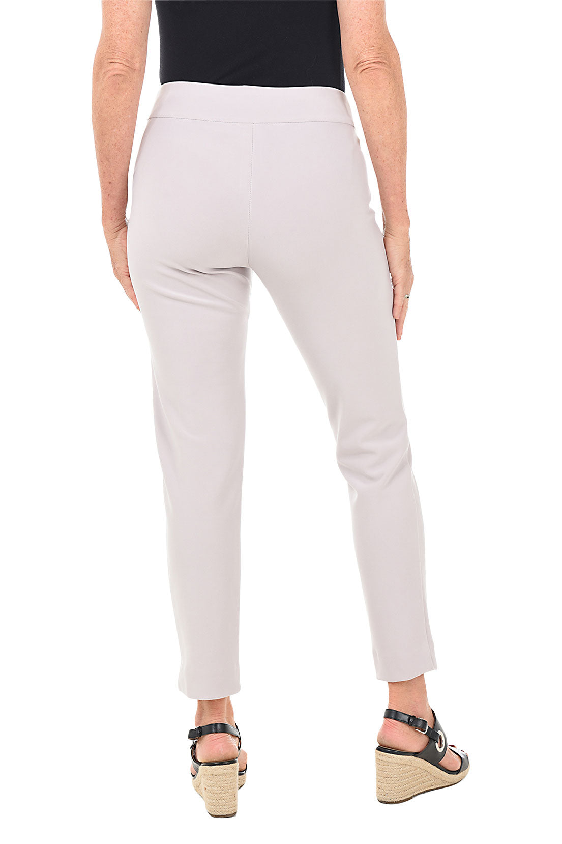 A back shot of a model wearing a pair of white microfiber pull-on ankle pants with an elastic waistband, displayed on a model wearing black top and heels