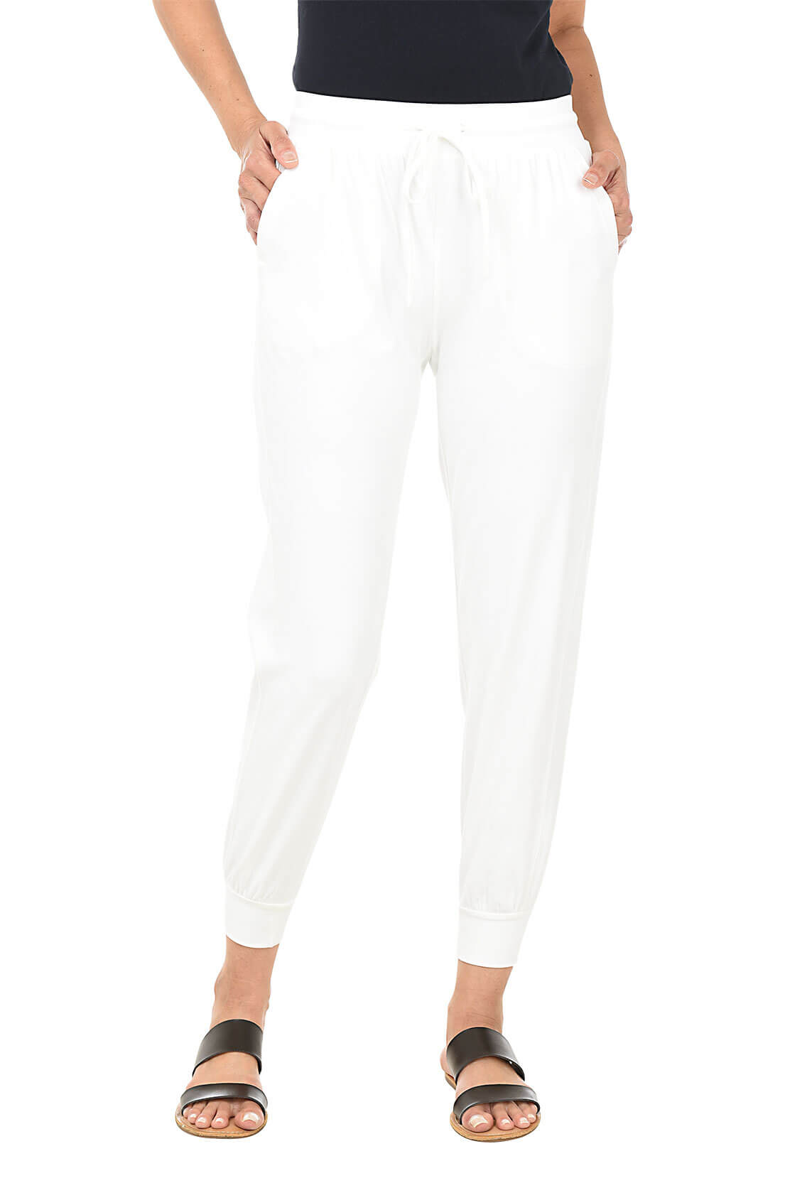 A front shot of a model wearing a pair of solid white ankle-length jogger pants with an elastic waistband and adjustable drawstring, featuring front patch pockets with a zippered coin pocket, flat back, relaxed fit through the leg, and rib-knit cuffs at the ankle.