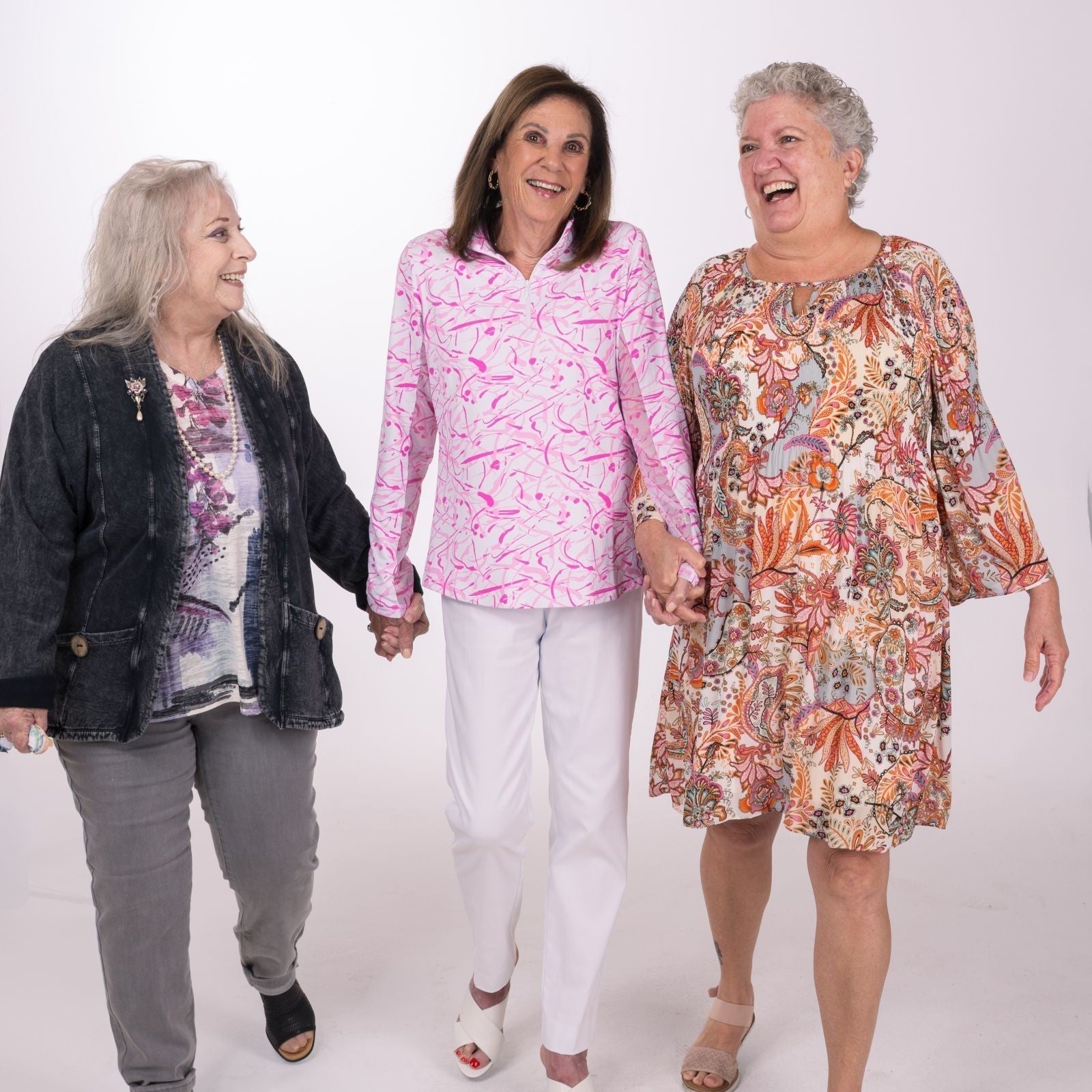 3 ladies wearing a top, sweater and pants, a sun shirt and a dress