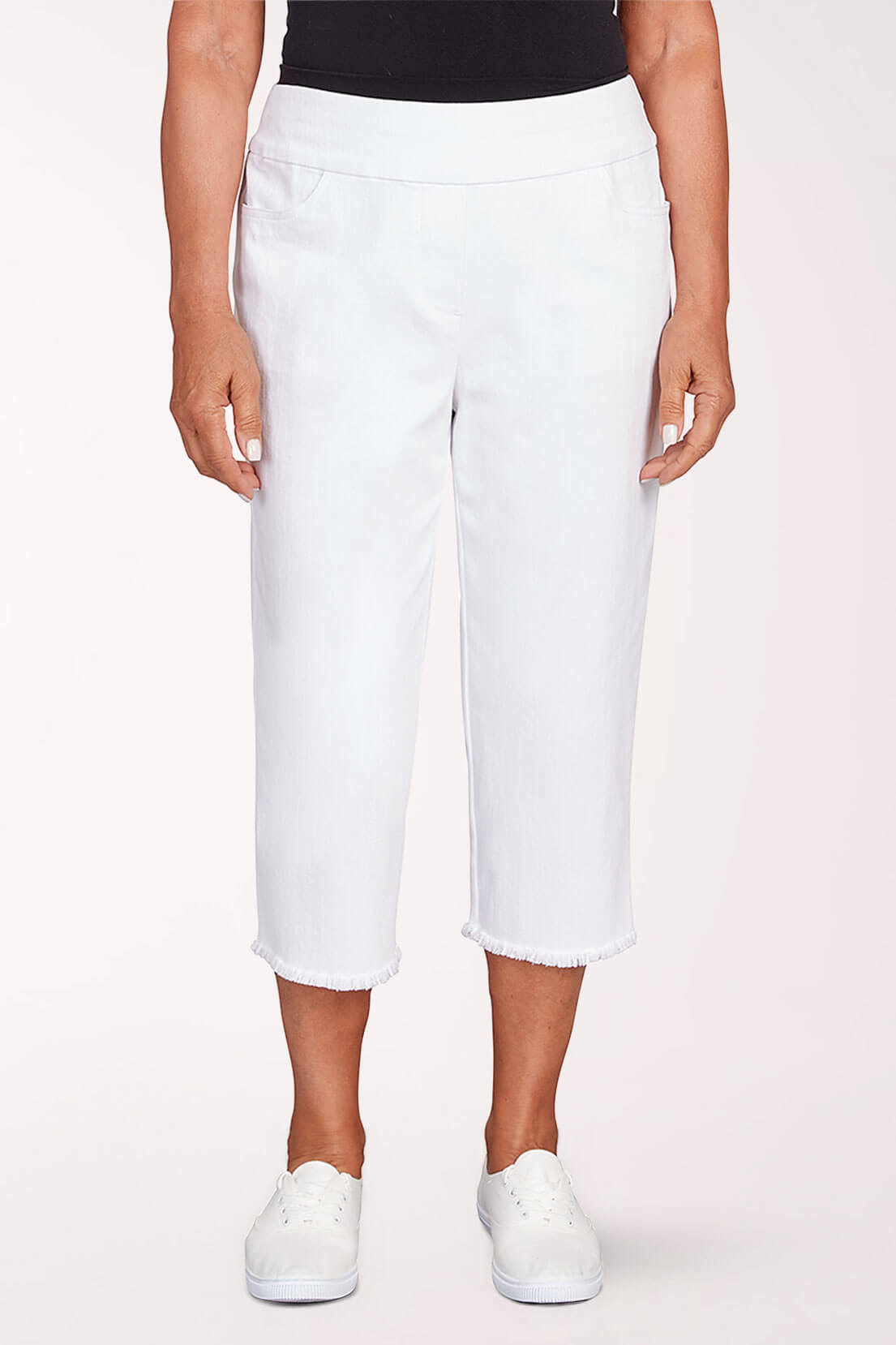 A woman wearing white denim capri pants against a light pink background