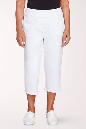 A woman wearing white denim capri pants against a light pink background