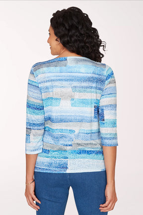 Woman wearing a 3/4 sleeve blue brushstroke top.