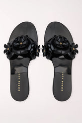 A pair of black patent jelly slide sandals by Jack Rogers, featuring large 3D floral embellishments across the straps with small gold-tone center details, shown from a top-down view on a light off-white background.
