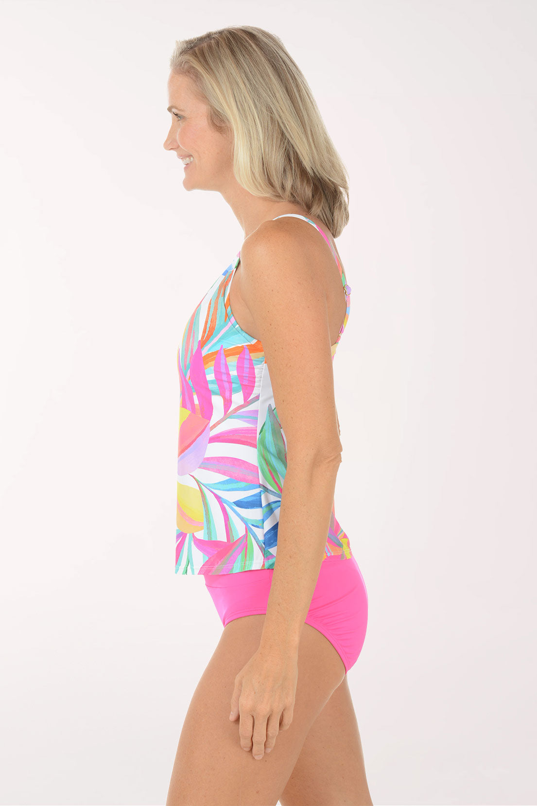 Woman wearing a colorful patterned tankini top with pink bottom on a white background. Side shot.