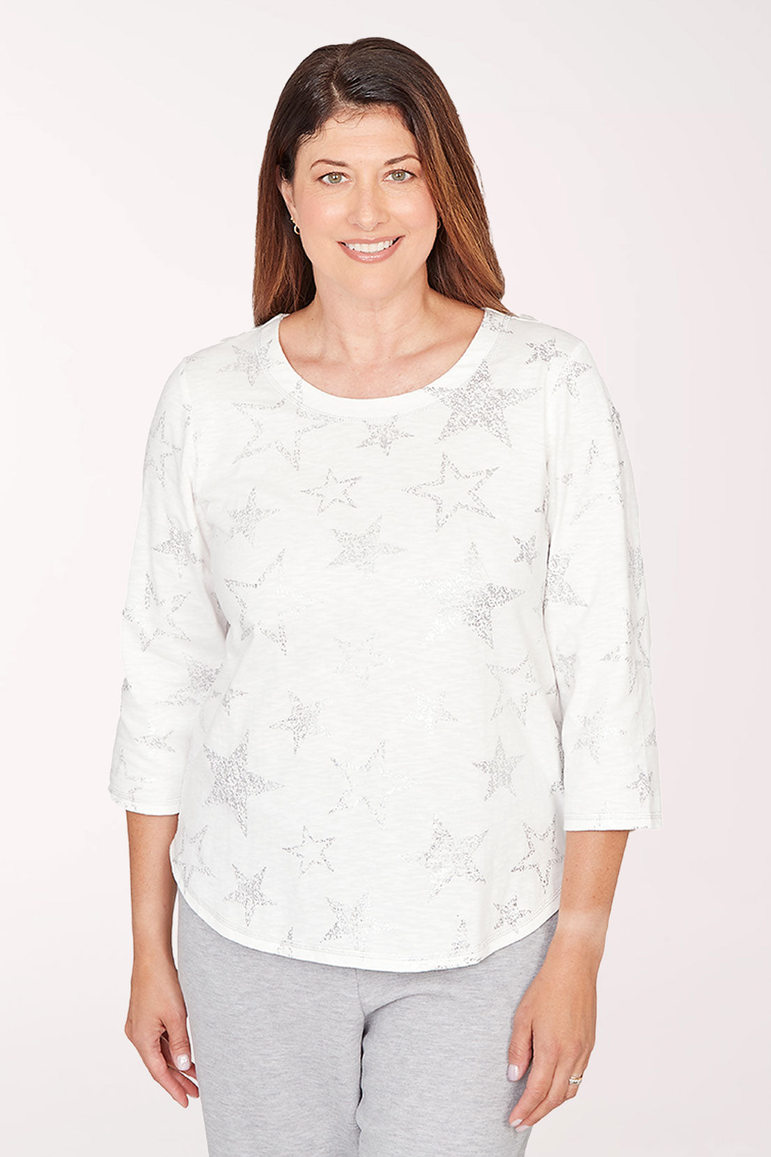 Woman wearing a white floral blouse and gray pants on a light pink background