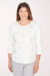 Woman wearing a white floral blouse and gray pants on a light pink background
