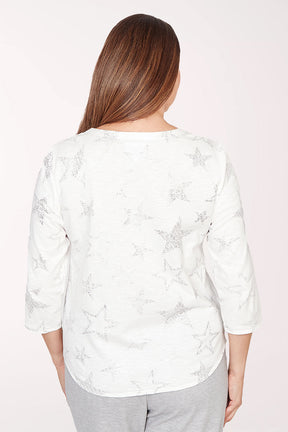 Woman wearing a white floral blouse and gray pants on a light pink background