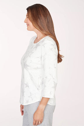 Woman wearing a white floral blouse and gray pants on a light pink background