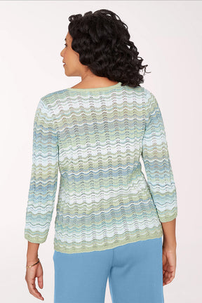 Woman wearing a patterned sweater and blue pants on a white background