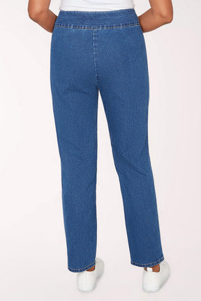 Person wearing blue jeans and white sneakers on a light pink background