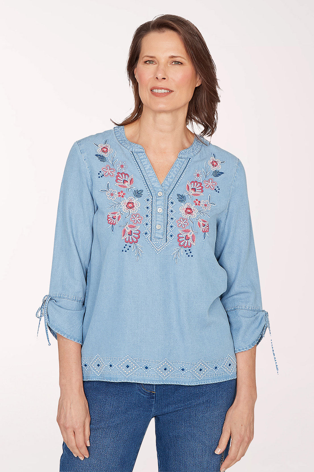 Woman wearing a light blue denim blouse with floral embroidery on a white background