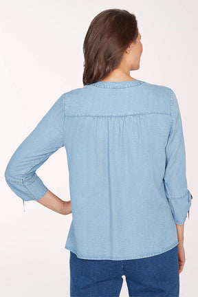 Woman wearing a light blue denim blouse with floral embroidery on a white background