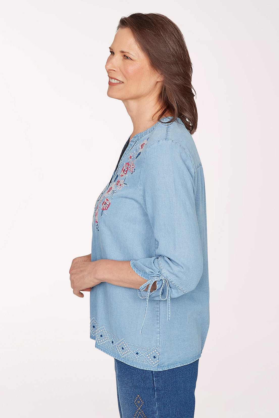 Woman wearing a light blue denim blouse with floral embroidery on a white background