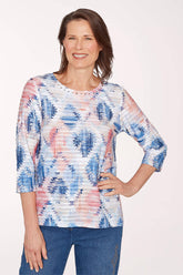 Woman wearing a colorful patterned top with blue jeans on a white background