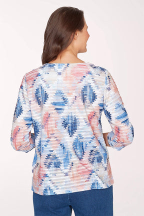 Woman wearing a colorful patterned top with blue jeans on a white background