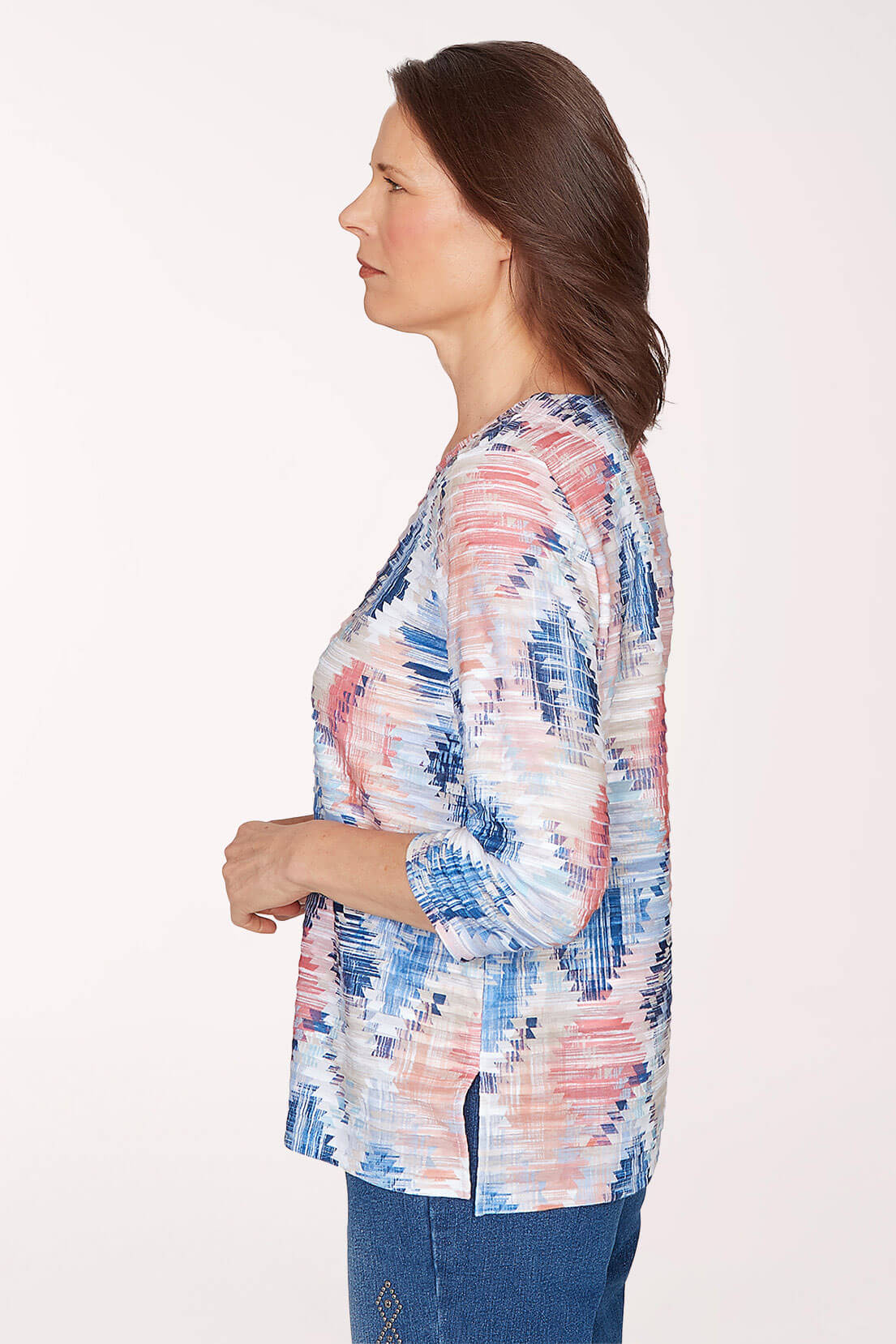 Woman wearing a colorful patterned top with blue jeans on a white background