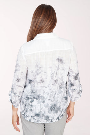 Woman wearing a light-colored floral blouse with rolled-up sleeves on a white background