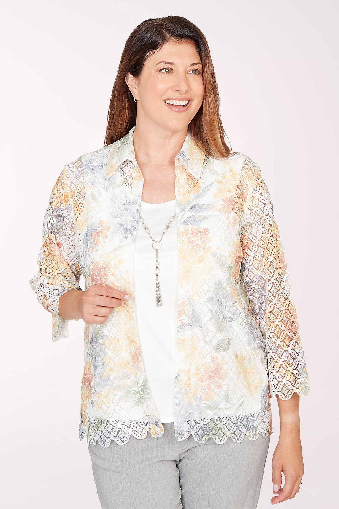 Woman wearing a floral lace kimono-style jacket over a white top on a white background