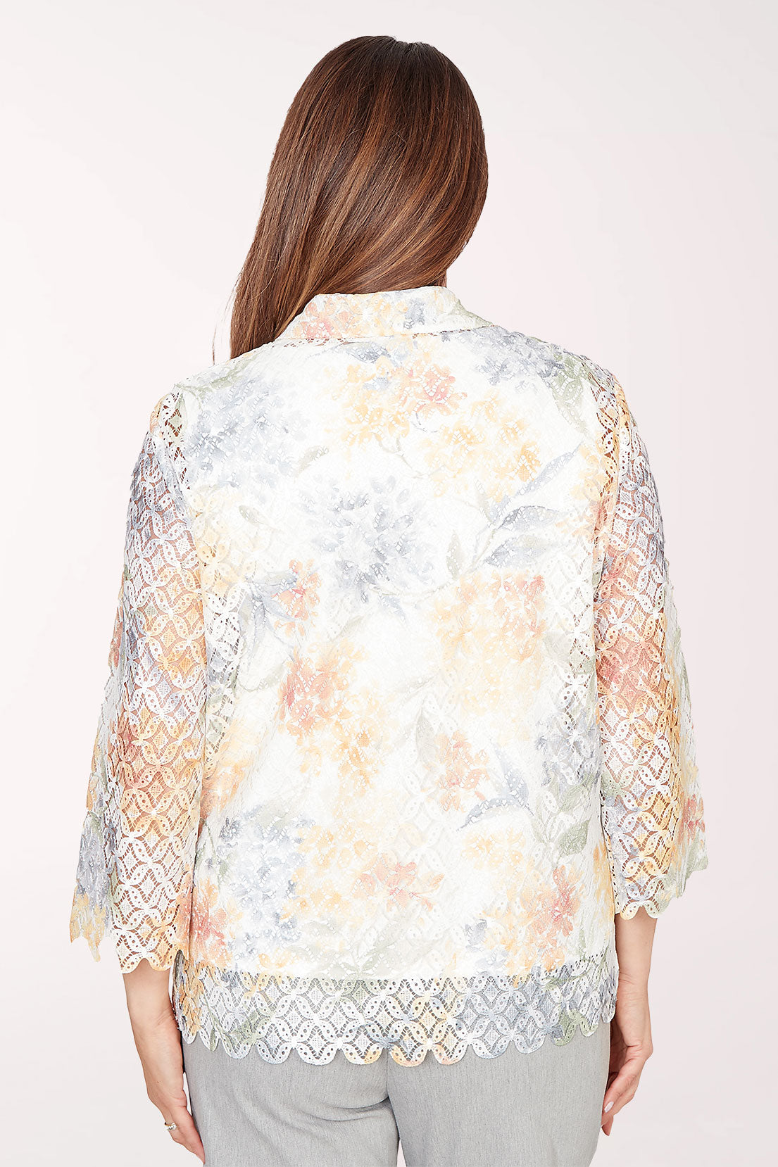 Woman wearing a floral lace kimono-style jacket over a white top on a white background