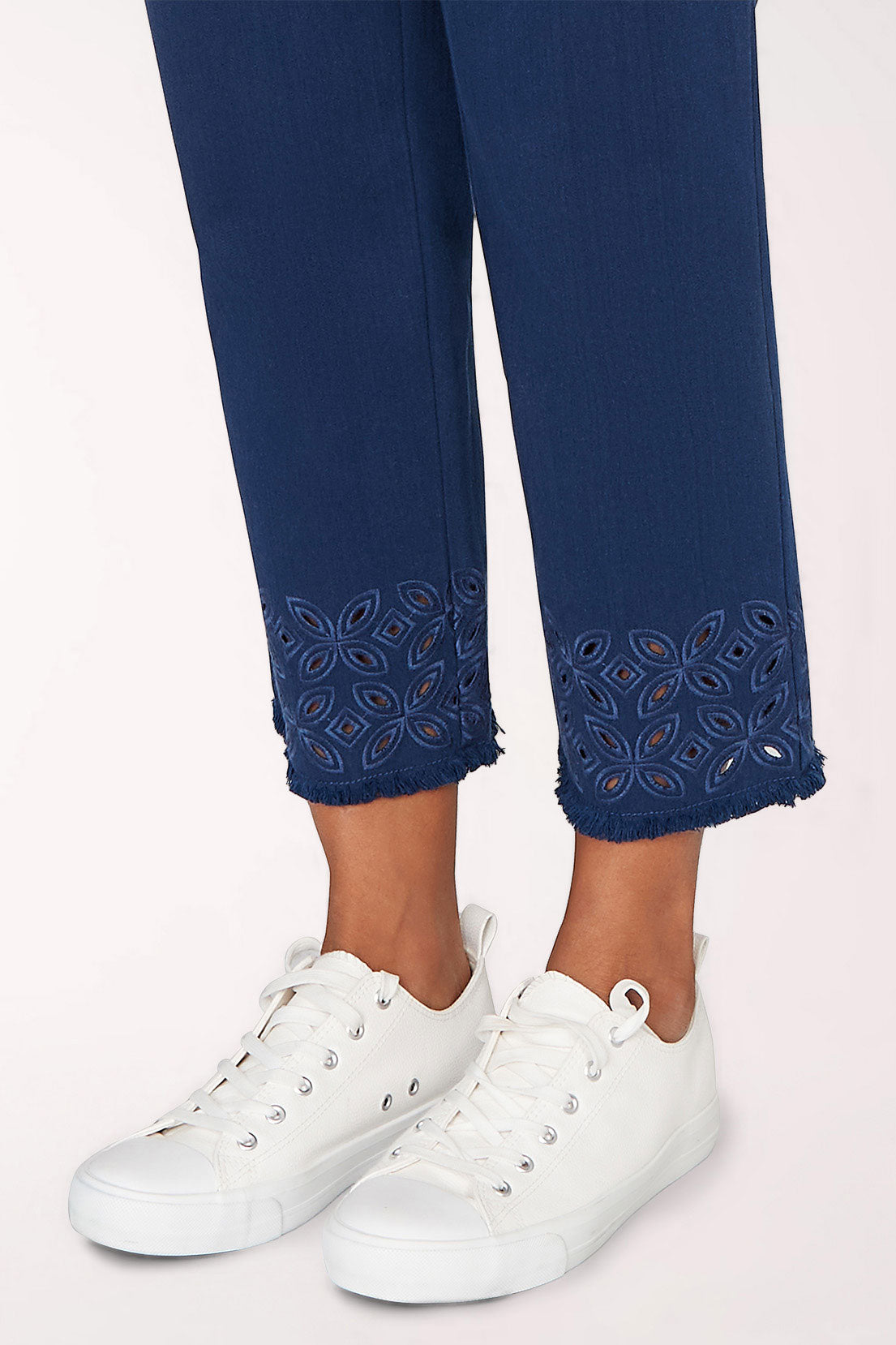 Navy blue pants with embroidered details and white sneakers on a light pink background