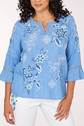 Woman wearing a blue embroidered blouse with white pants on a white background