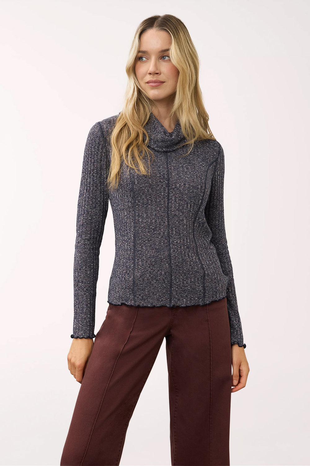 A woman modeling a dark gray ribbed knit cowl-neck sweater paired with dark brown pants, photographed against a plain light background.