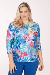 Woman wearing a colorful floral print top with blue pants on a white background