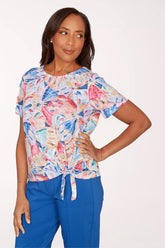 Woman wearing a colorful patterned top and blue pants on a white background