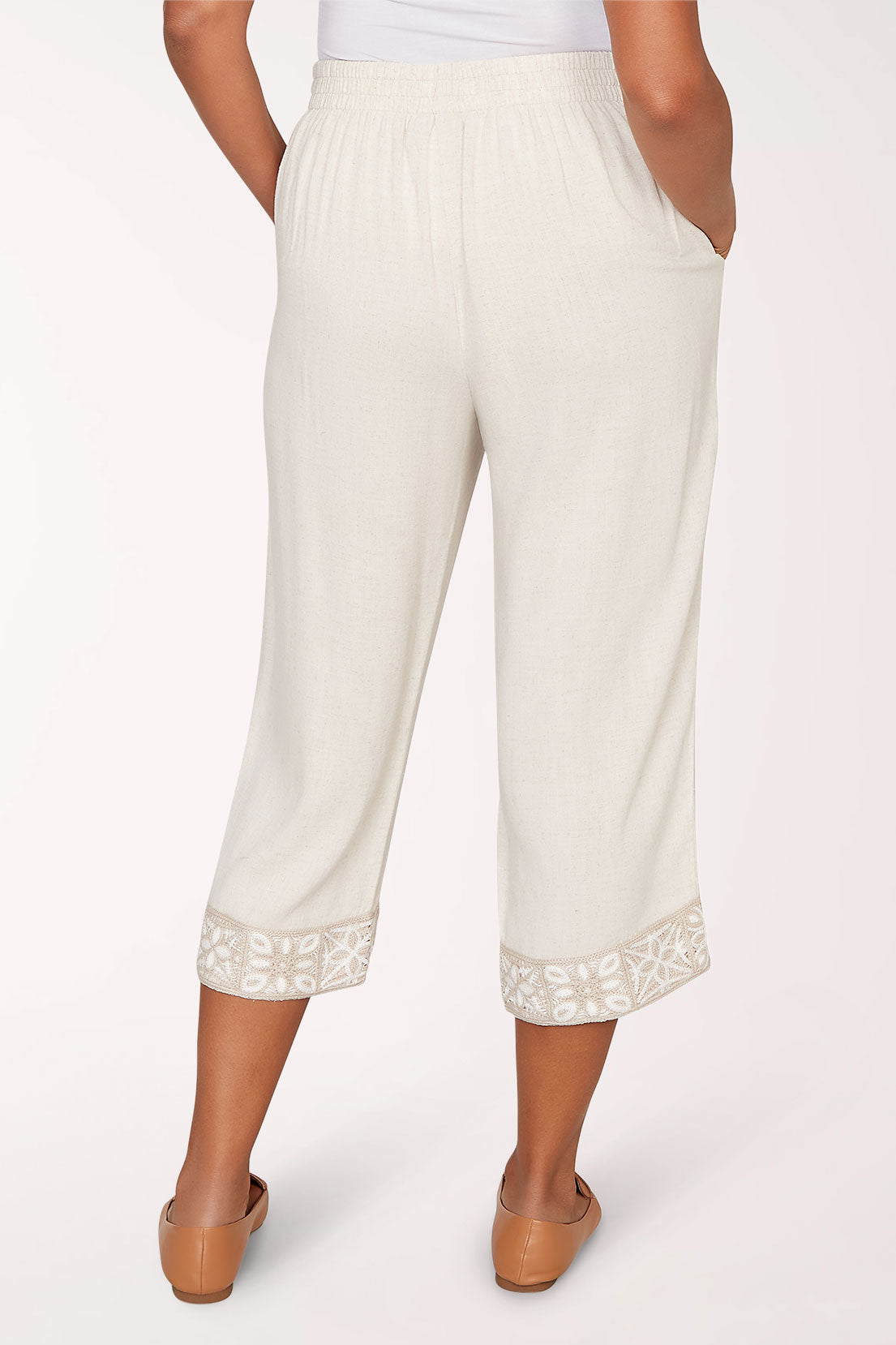 Person wearing white pants with lace cuffs on a white background