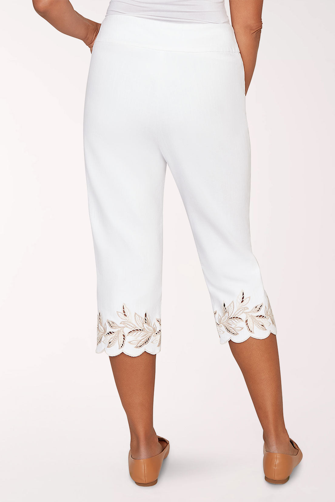Person wearing white pants with lace trim and brown shoes on a white background
