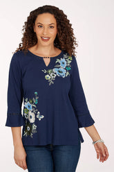 Woman wearing a navy 3/4 sleeve top with a floral design