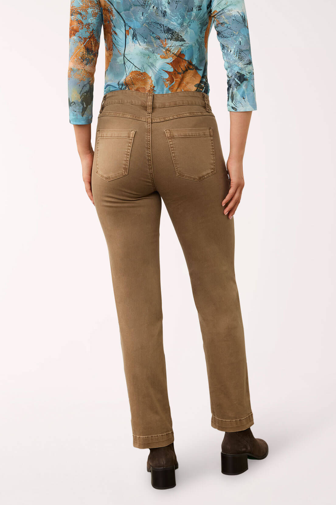 A model shown from the back wearing brown straight-leg jeans, a blue and orange patterned long-sleeve top, and dark brown ankle boots against a plain white studio background.