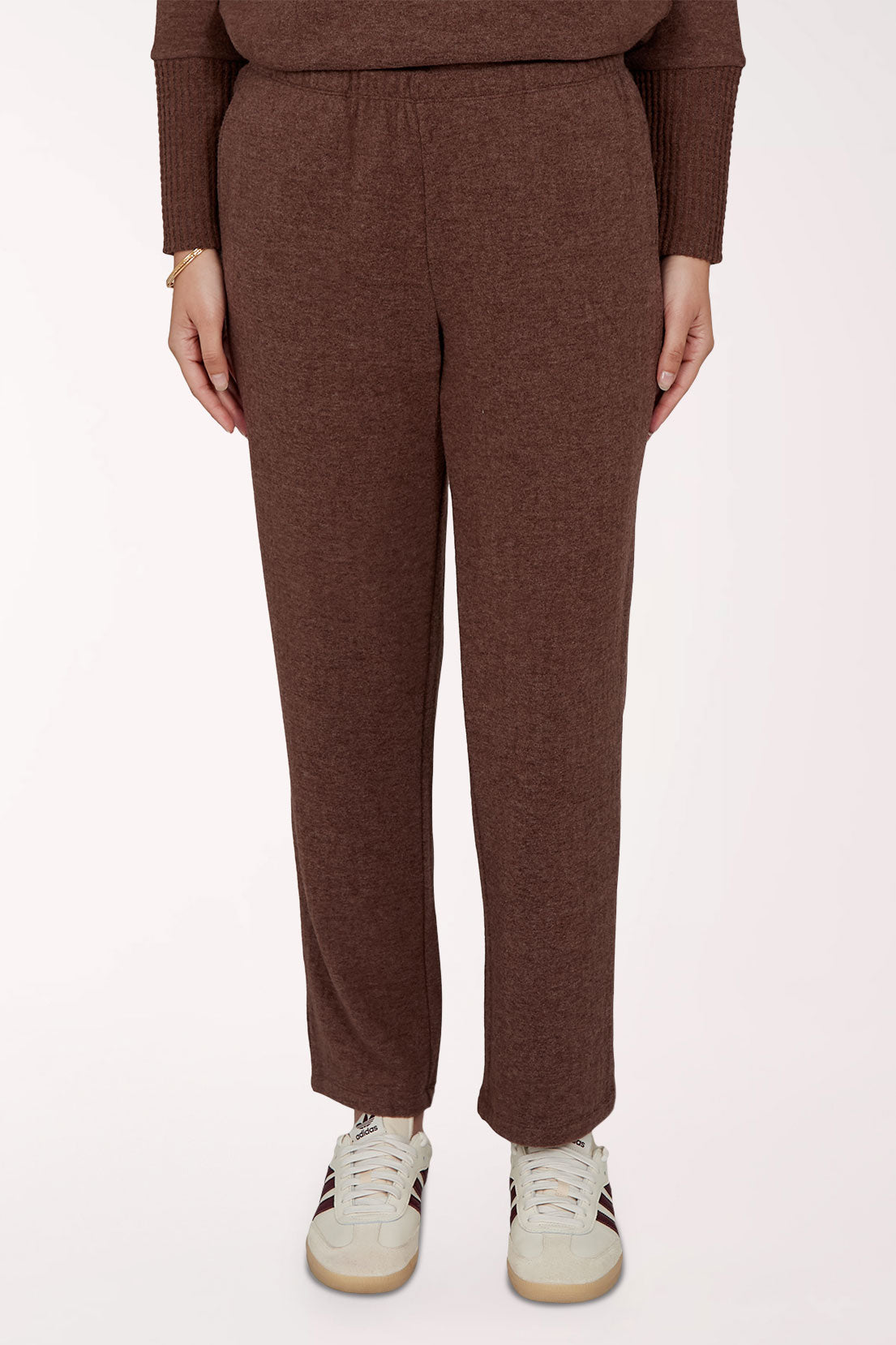 A person wearing a matching brown knit sweater and relaxed-fit knit pants, paired with white sneakers, shown from the chest down against a plain light background.