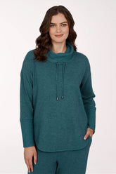 A woman wearing a teal green knit mock neck sweater with a drawstring detail and matching knit pants, photographed against a clean white studio background.