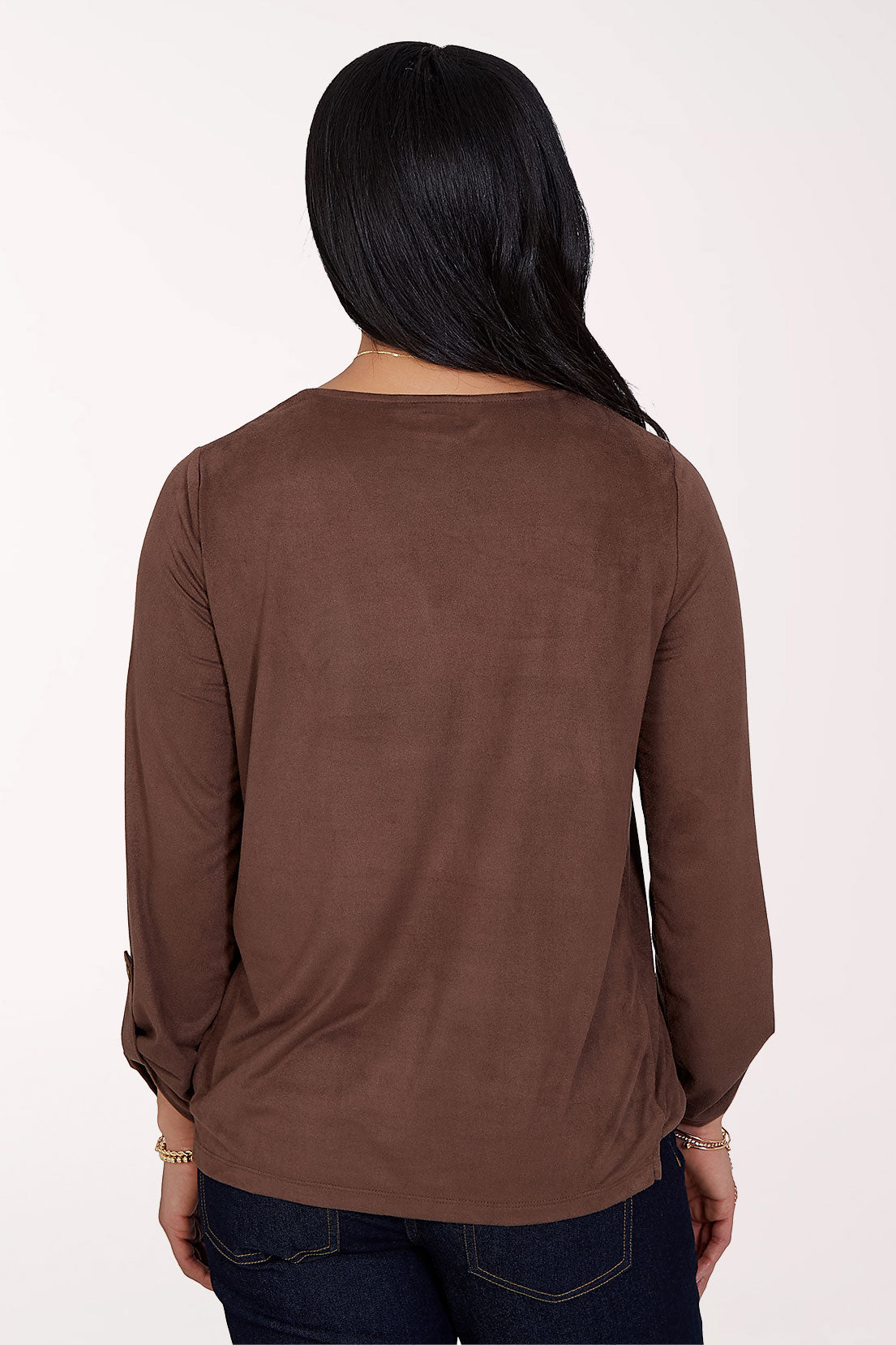 A woman modeling a brown long-sleeve wrap-style blouse with a V-neckline, paired with dark blue jeans, against a plain light background.