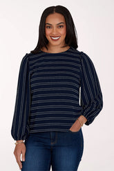 A woman modeling a navy blue long-sleeve top with thin white dotted horizontal stripes, paired with dark blue jeans, against a plain white studio background.
