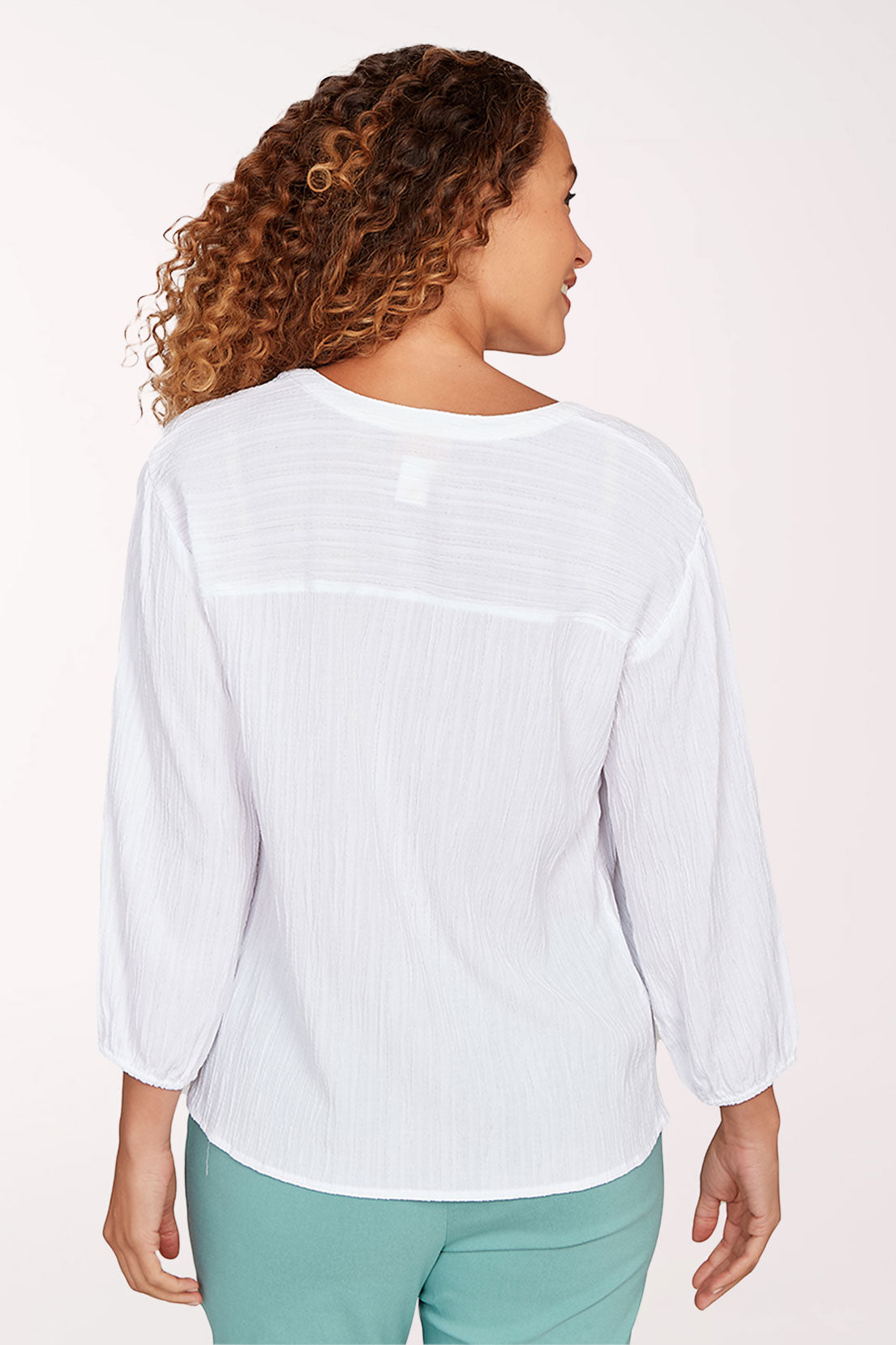 Woman wearing a white blouse with a subtle pattern on a plain background