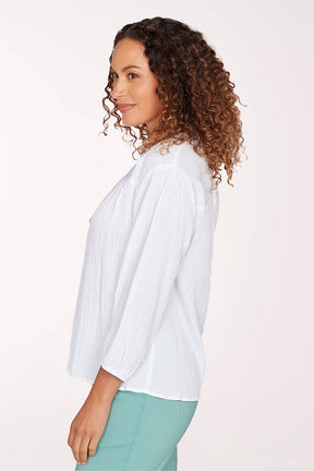 Woman wearing a white blouse with a subtle pattern on a plain background