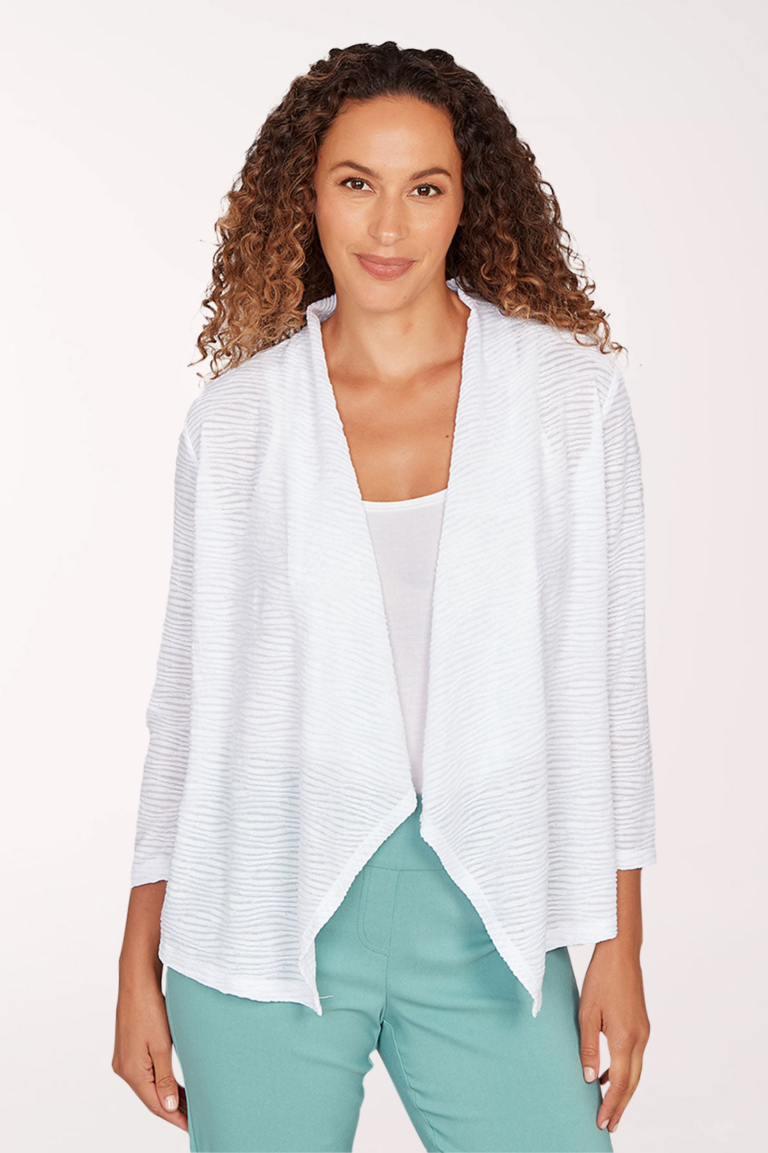 Woman wearing a white open-front cardigan over a white top and green pants on a light pink background