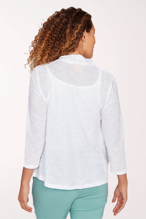 Woman wearing a white open-front cardigan over a white top and green pants on a light pink background